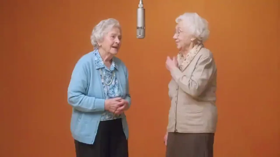 Two women performing beneath a suspended microphone in an orange studio